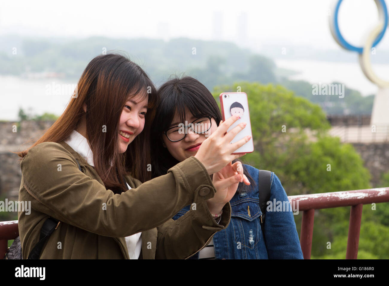Two smiling Chinese young girls with long hair posing for a selfie with a smart phone at Nanjing Stock Photo