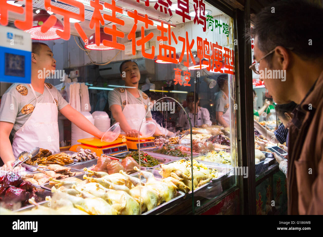 Customer watching Chinese butchers selling meat at a indoor market in Nanjing, China Stock Photo