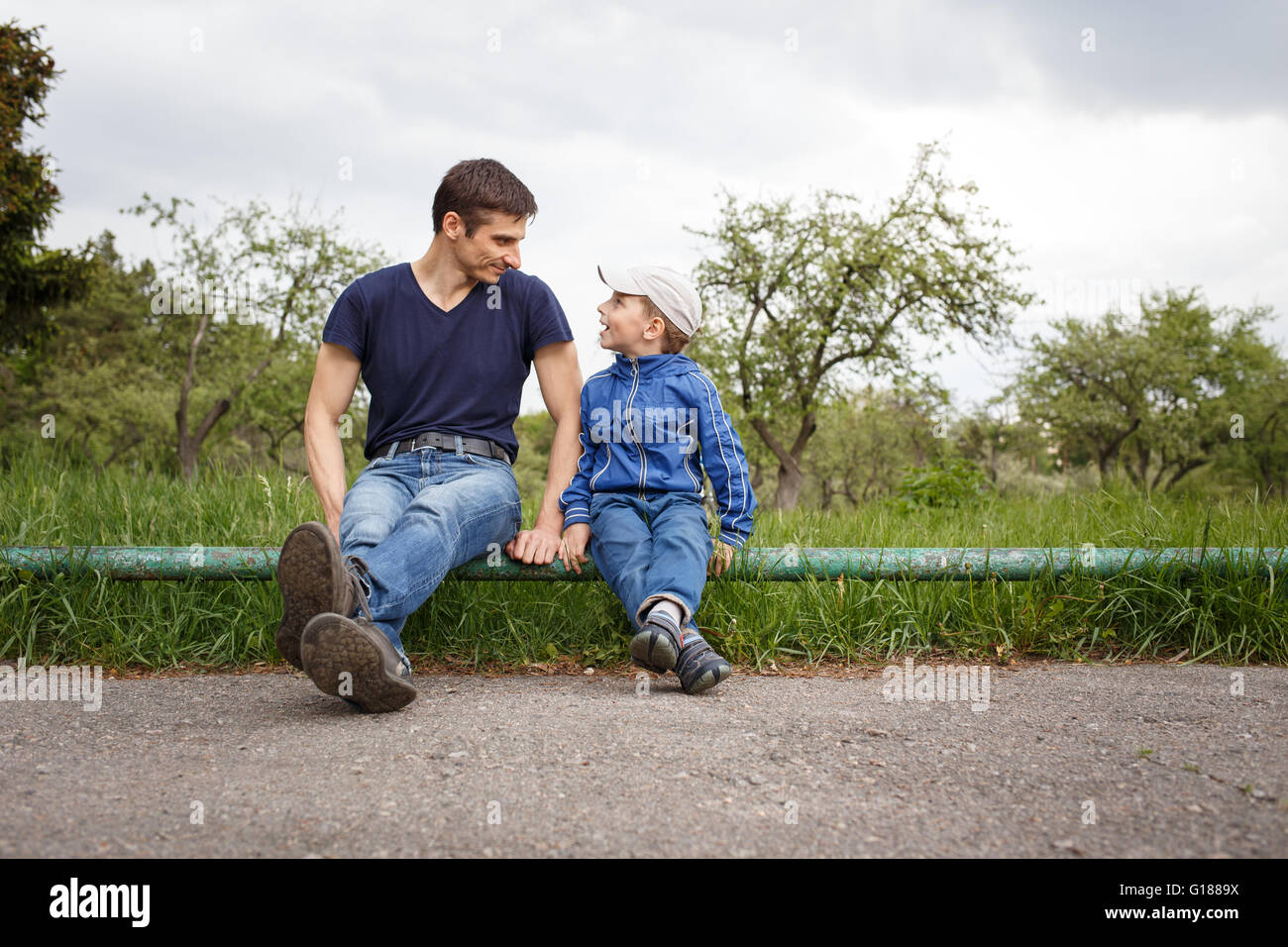 Happy father and son sitting in the park. Smiling young man spending time together with his son Stock Photo