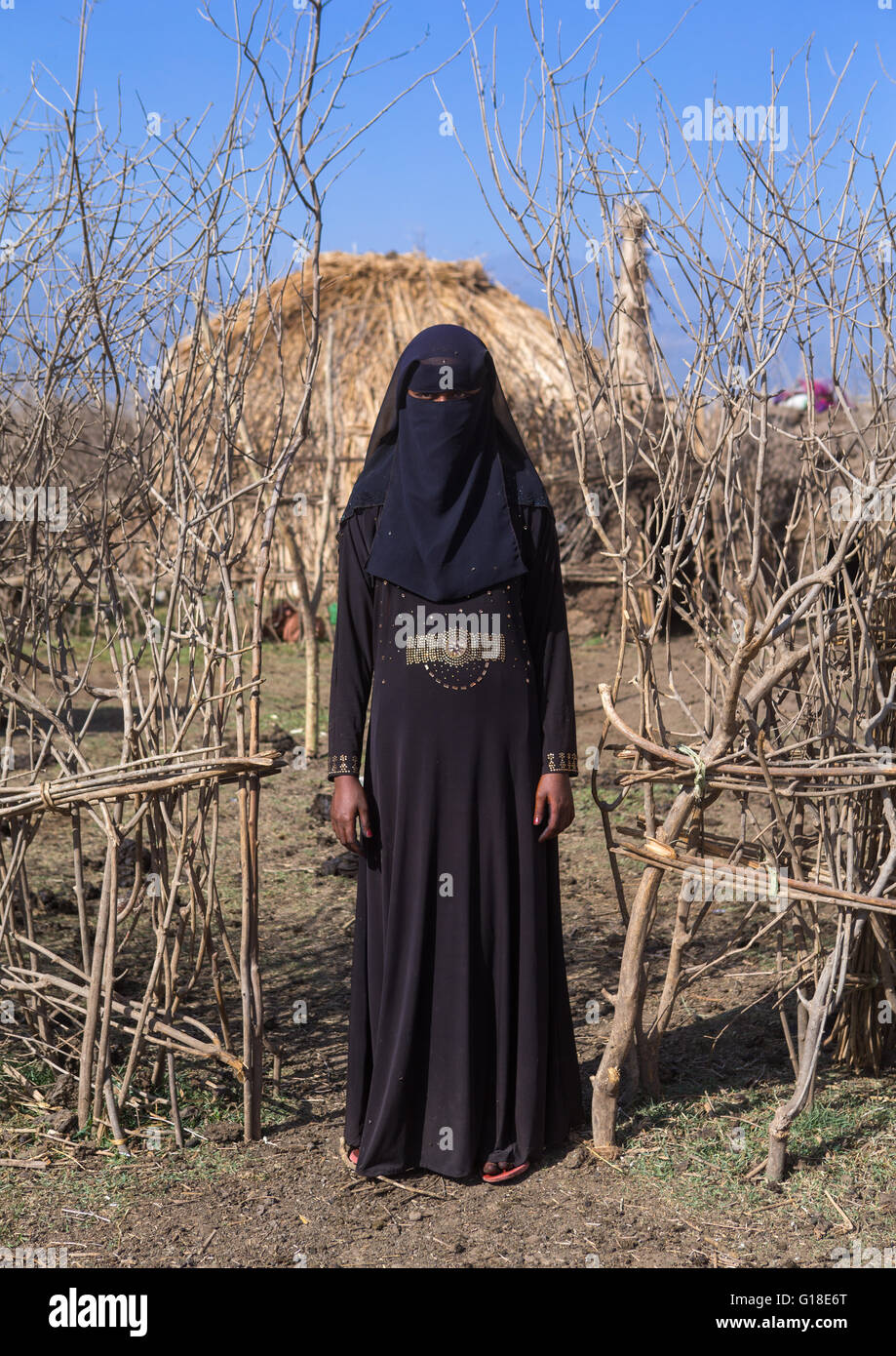 An ethiopian oromo woman dressed in black burqa stands in front of her hut, Amhara region, Artuma, Ethiopia Stock Photo