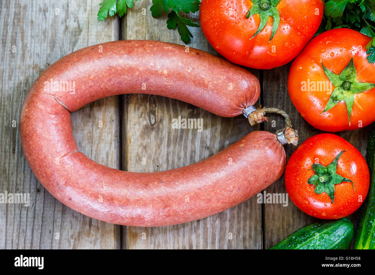 Beef sausage on wooden background with parsley, cucumber and tomato. Flat lay Stock Photo