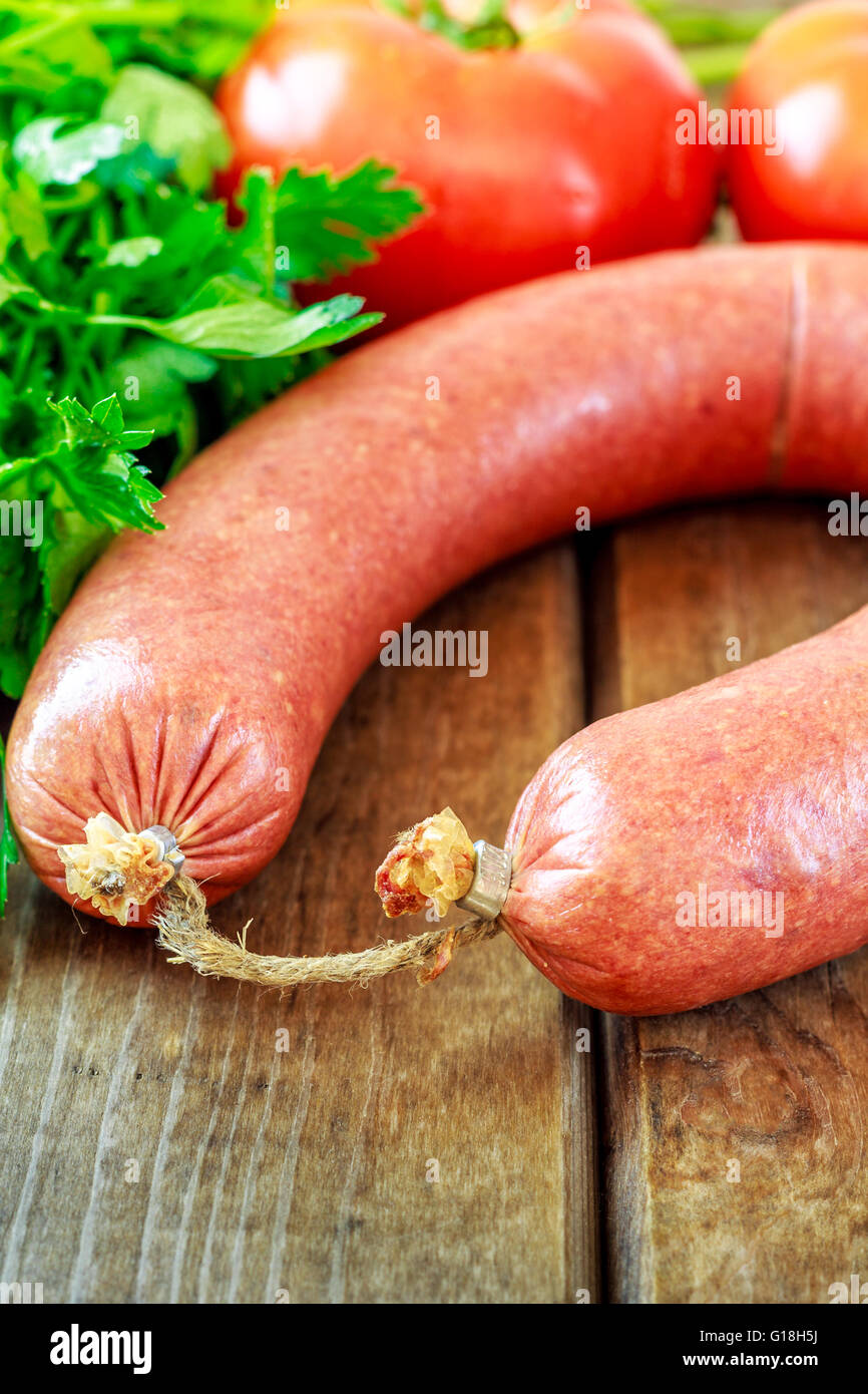 Beef sausage on wooden background with parsley and tomato Stock Photo