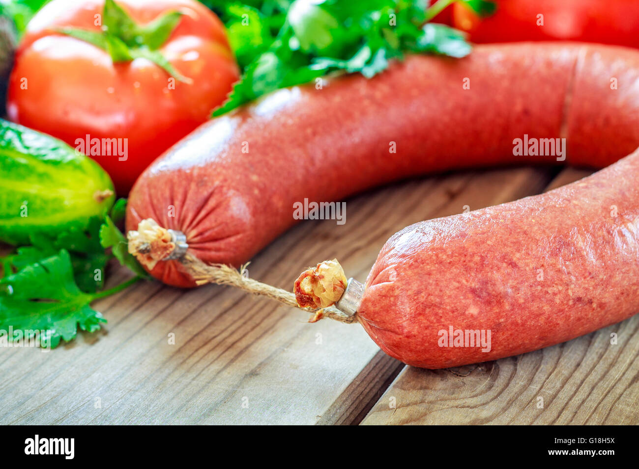 Beef sausage on wooden background with parsley, cucumber and tomato Stock Photo