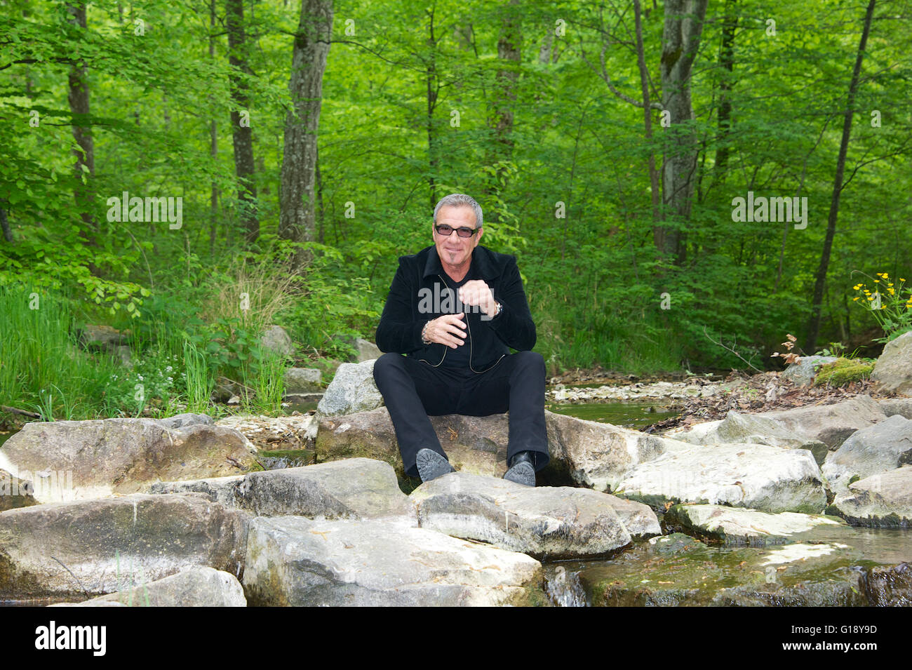 Seeshaupt, Germany. 10th May, 2016. dpa EXCLUSIVE - Tico Torres, drummer of Bon Jovi, sits between rocks after a presentation of his 'Rock Star Baby' fashion collection at the Lupaco Concept Store in Seeshaupt, Germany, 10 May 2016. Photo: Ursula Dueren/dpa/Alamy Live News Stock Photo