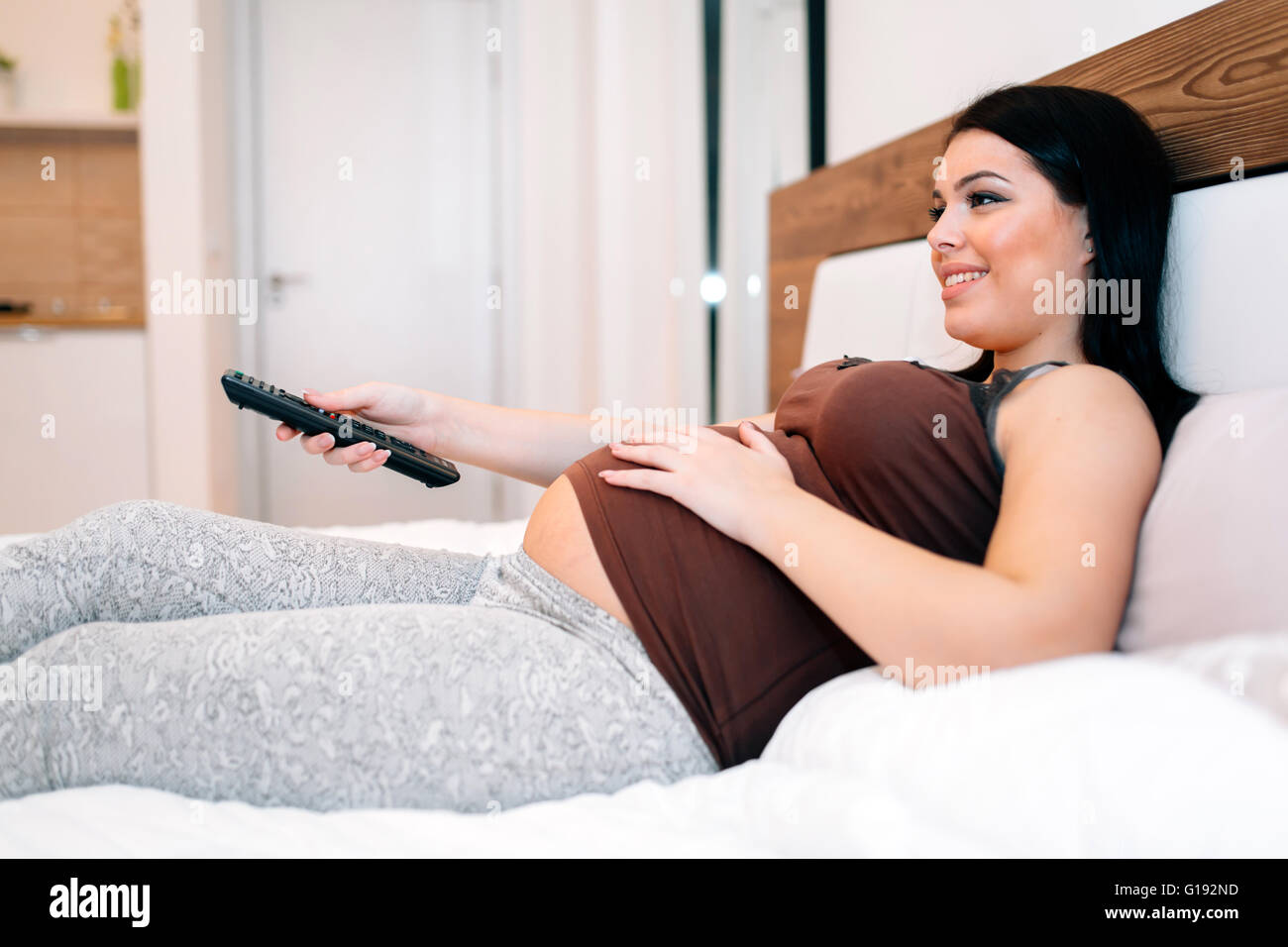 Beautiful pregnant woman watching TV at home and resting Stock Photo