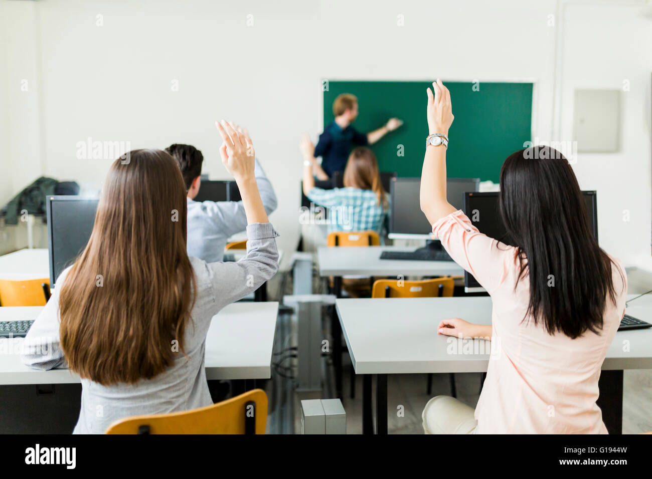 Young students raising hands in a classroom showing they are ready Stock Photo