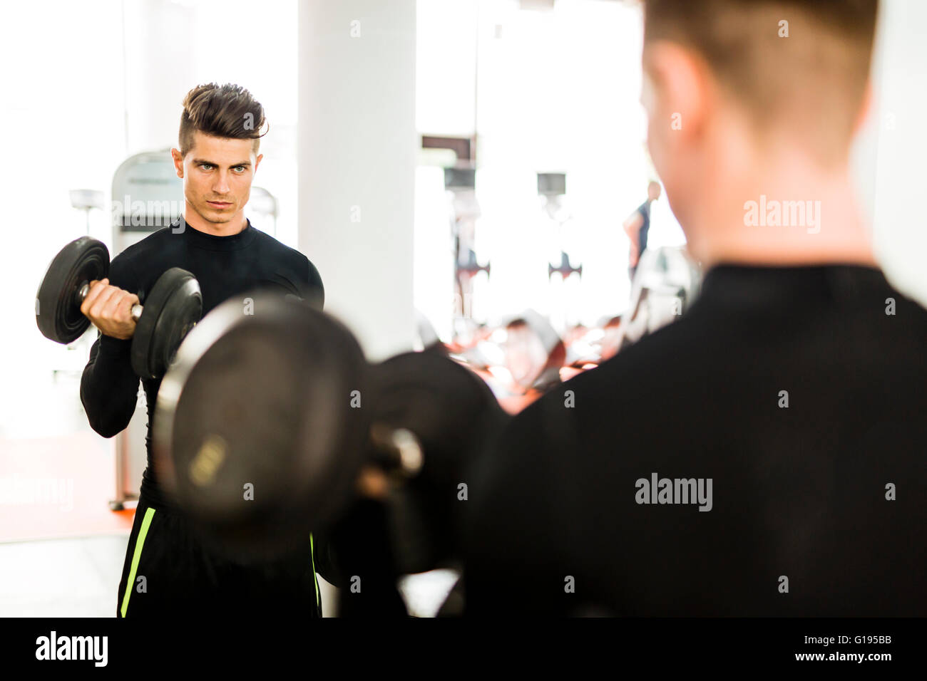 Young muscular man working out in a gym and lifting weights with his reflection showing in a mirror Stock Photo