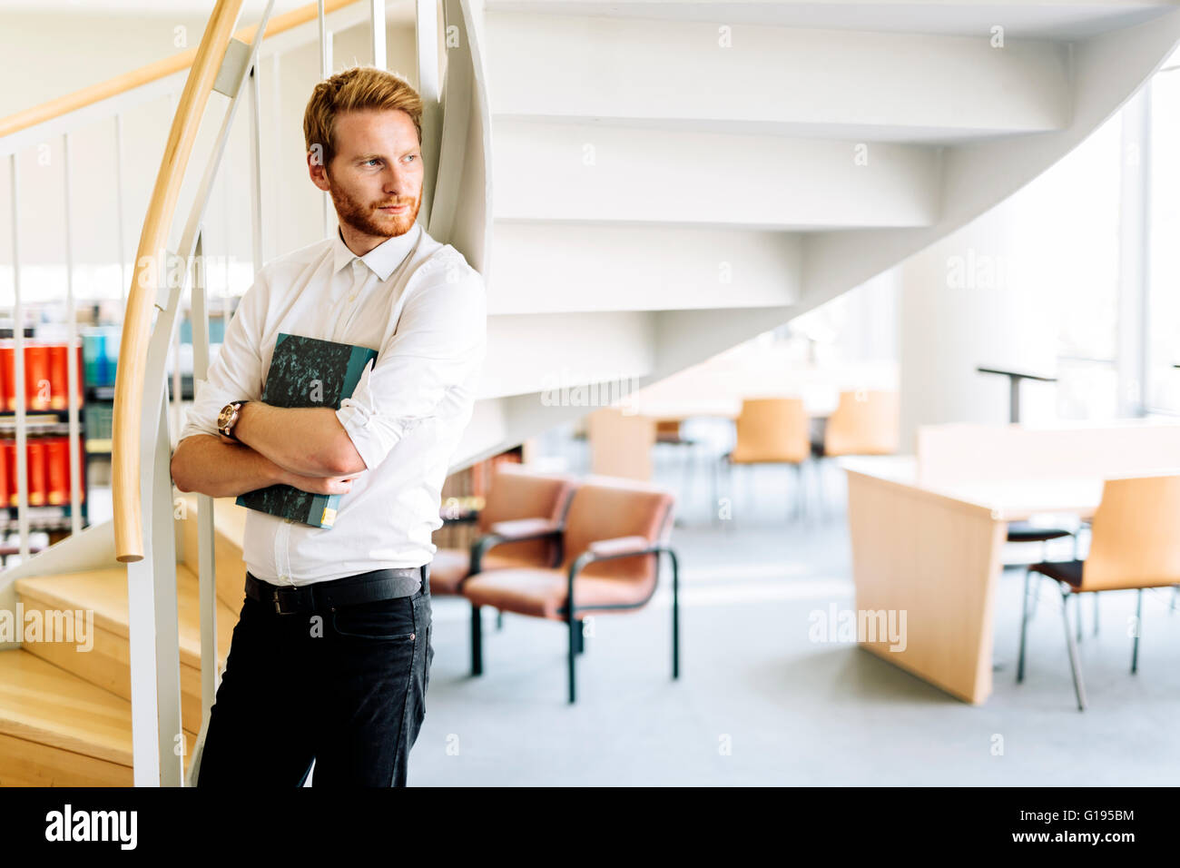Handsome smart guy reading a book in a library Stock Photo