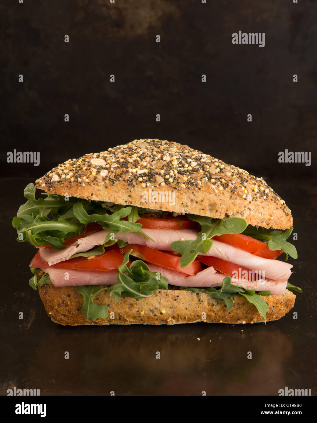 rustic ham salad sandwich in seeded bread roll against dark background