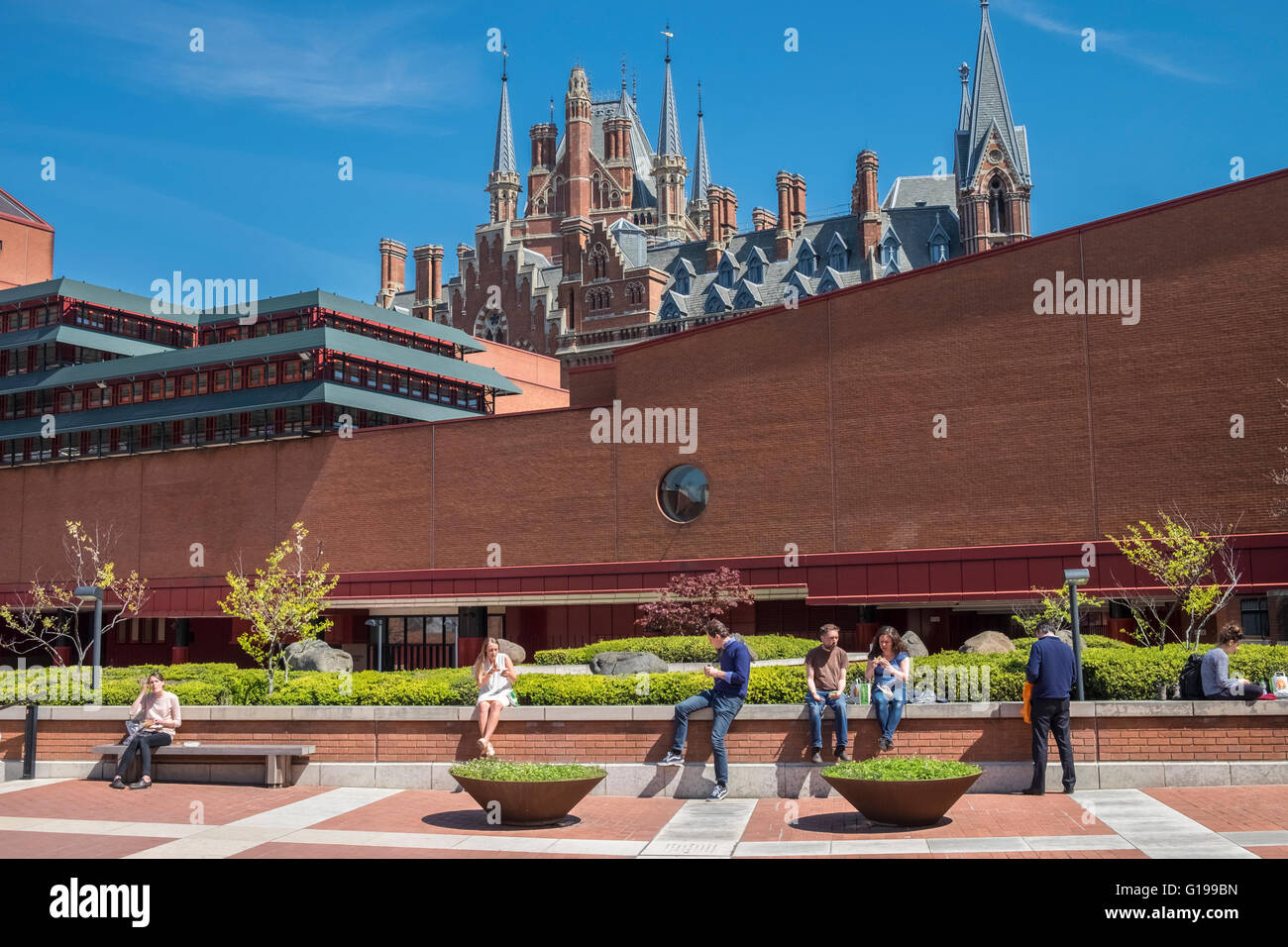 People sitting in British Library grounds, Euston Road, London, UK, with St Pancras Renaissance Hotel building in the background Stock Photo