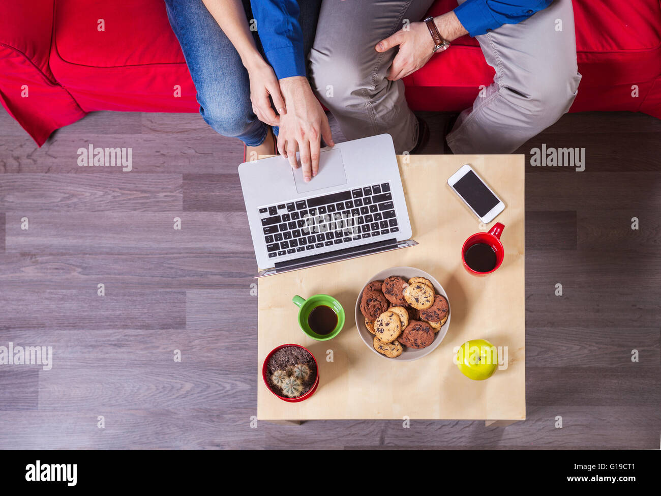Young couple using laptop while sitting on couch Stock Photo - Alamy