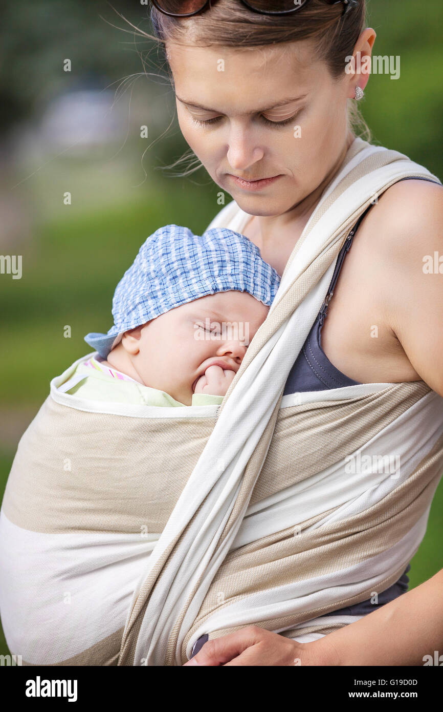 Sleeping toddler boy in sling, mother carrying son outdoors Stock Photo