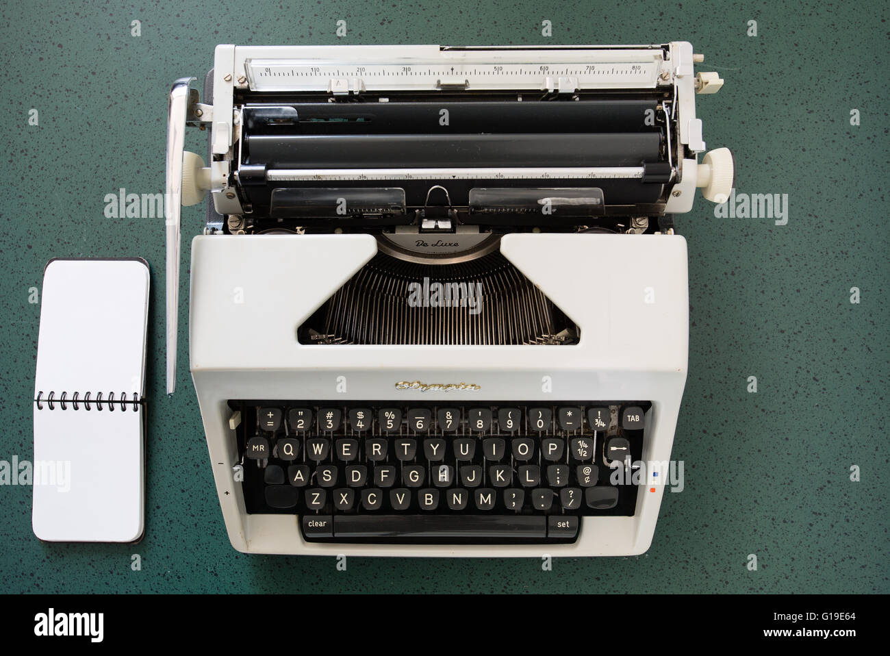 Portable metal typewriter, circa 1970, on a green desk with a notepad