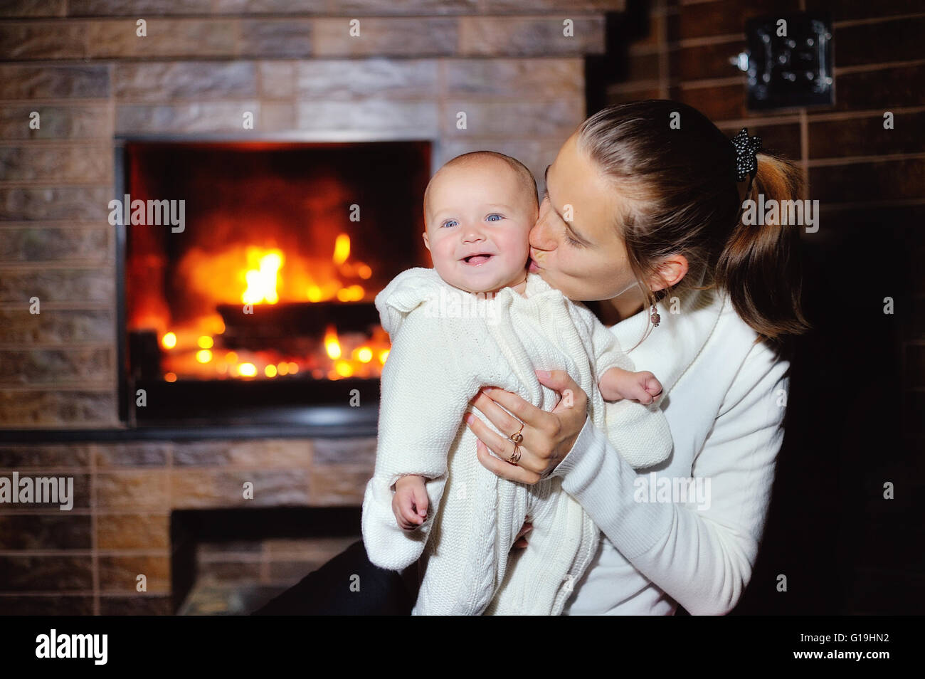 Mom kissing baby by the fireplace at home Stock Photo