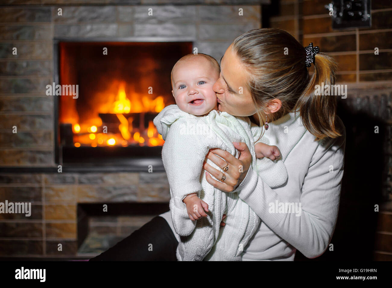 Mom kissing baby by the fireplace at home Stock Photo
