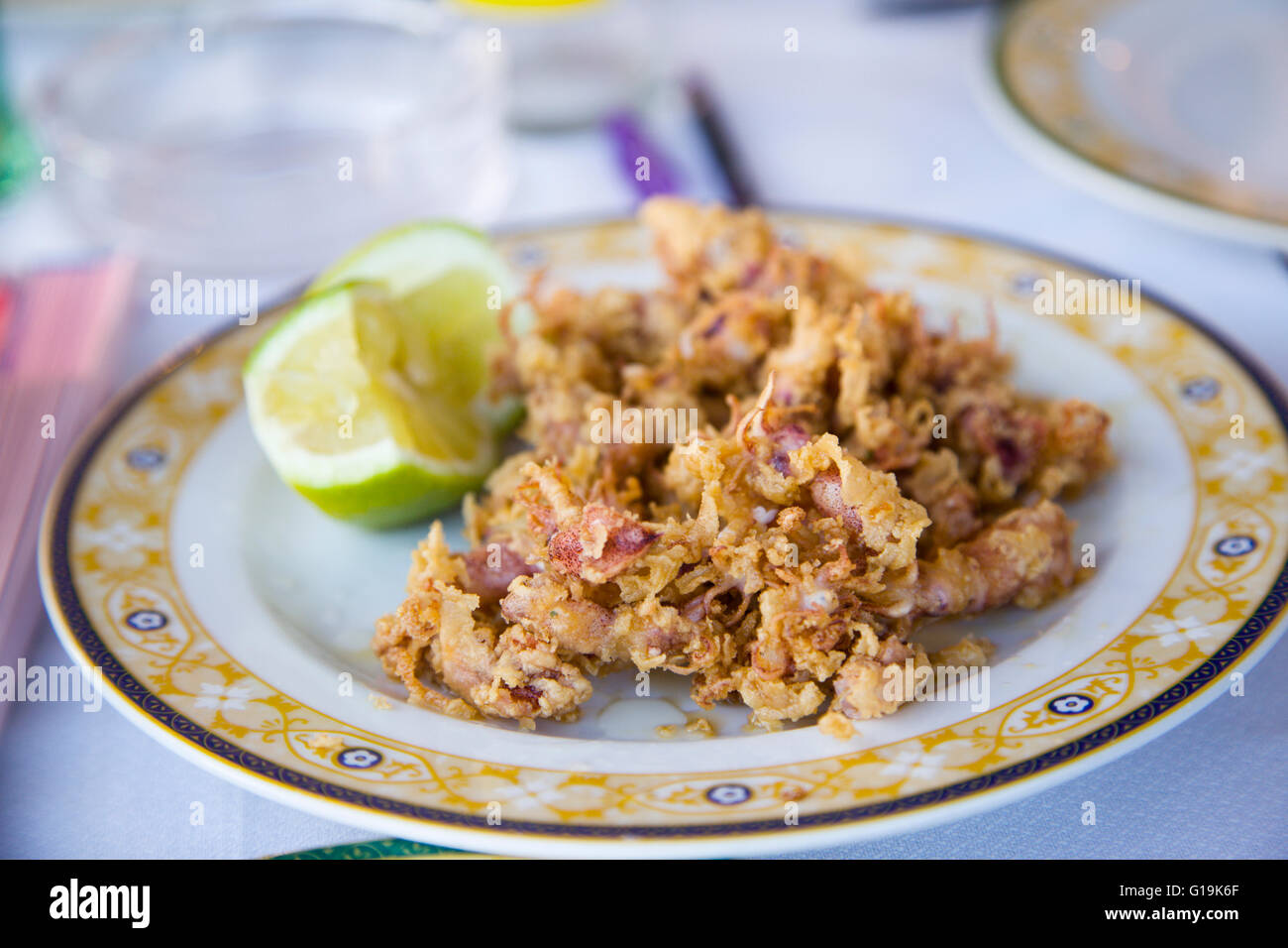 Deep fried baby squid in chili batter, with lime segments on a plate at