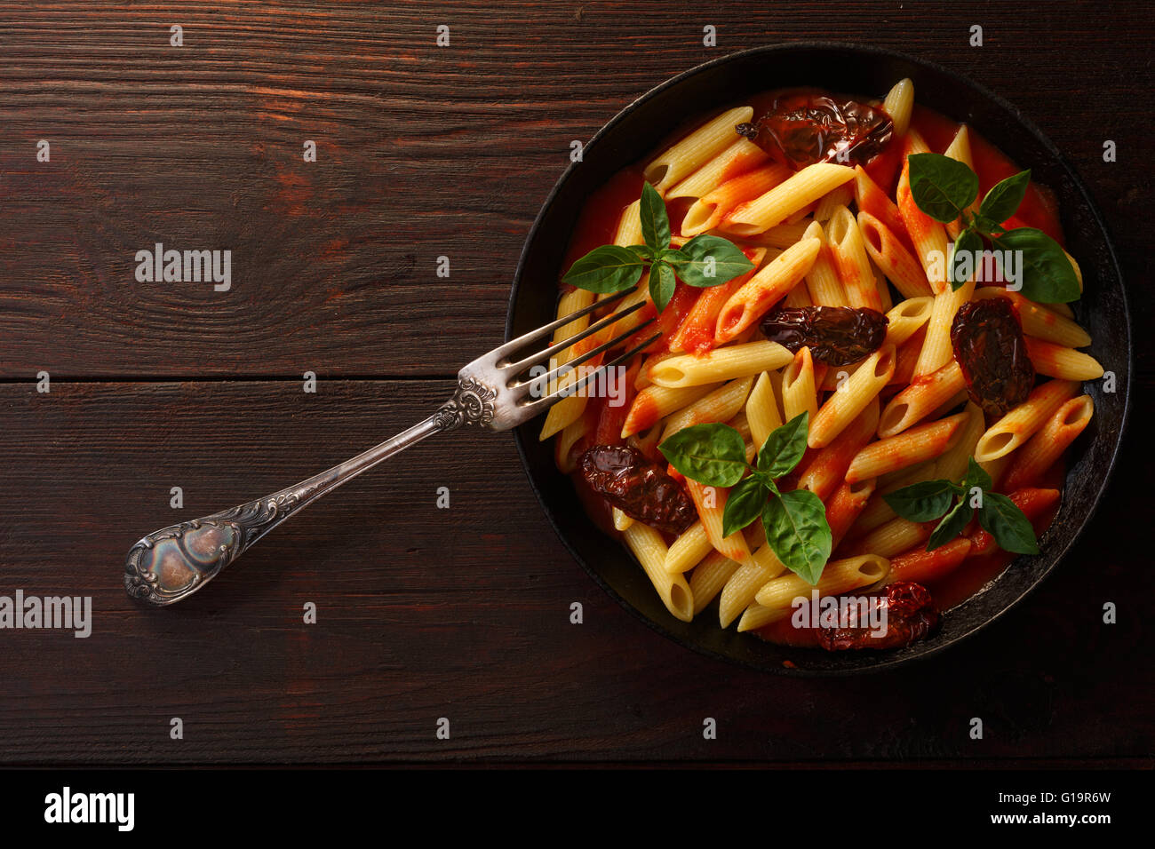 Pasta penne rigate with tomato sauce and basil leaves on wooden table. Top view, flat lay Stock Photo