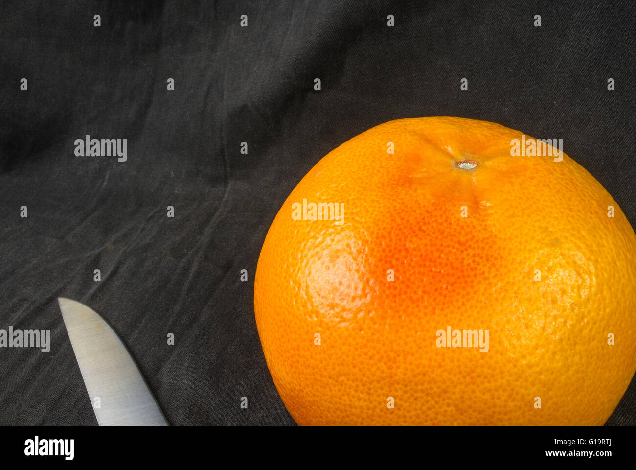 a large grapefruit with a knife on a black textile background Stock
