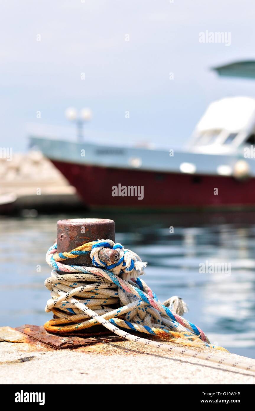 Marine rope on mooring bollard in port of Podgora, Croatia.  Blurred ship on background Stock Photo