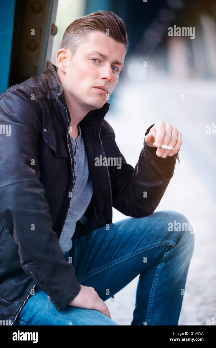 blond man in leather jacket smoking a cigarette Stock Photo