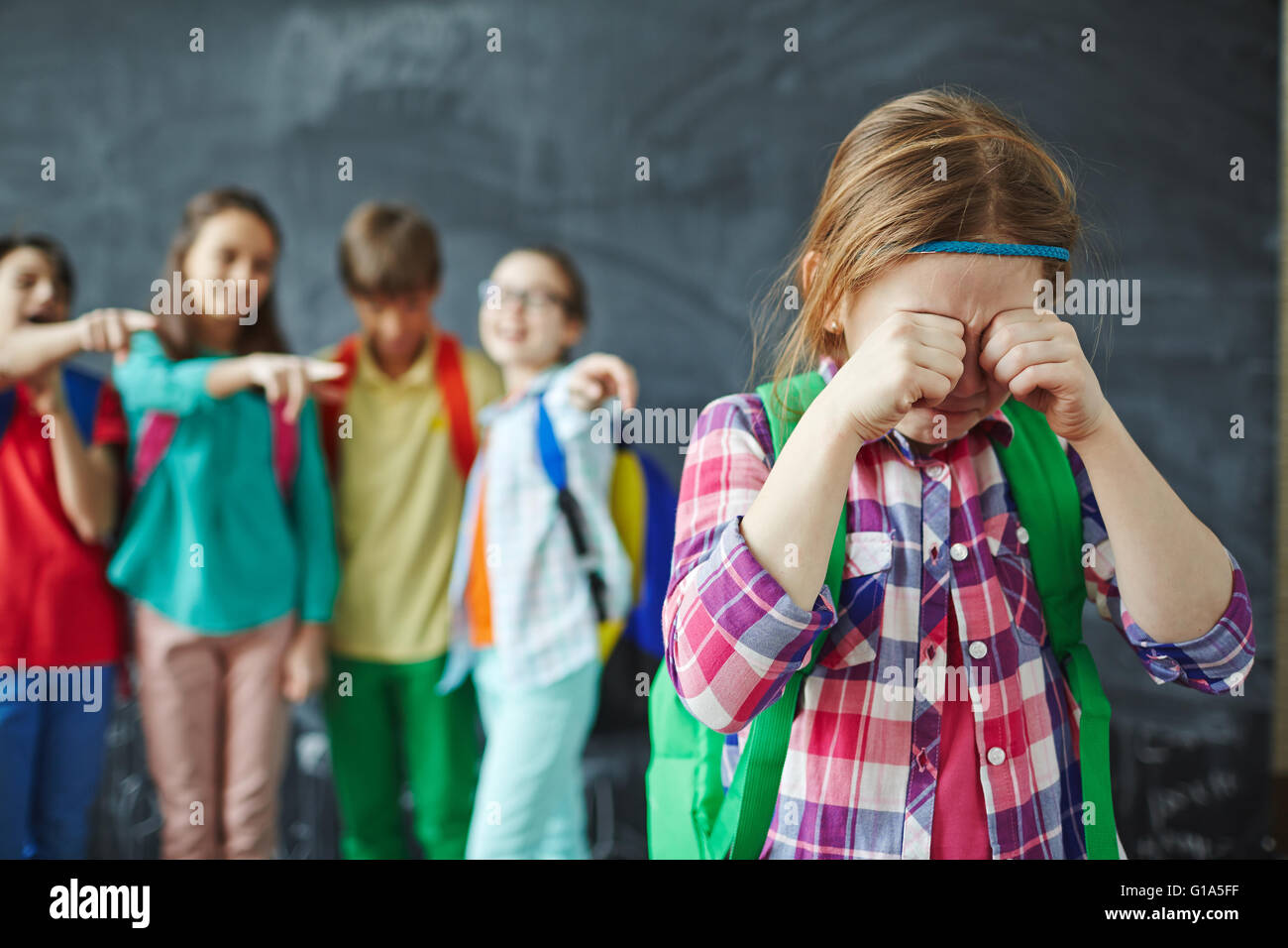 Schoolgirl crying while classmates teasing her on background Stock Photo