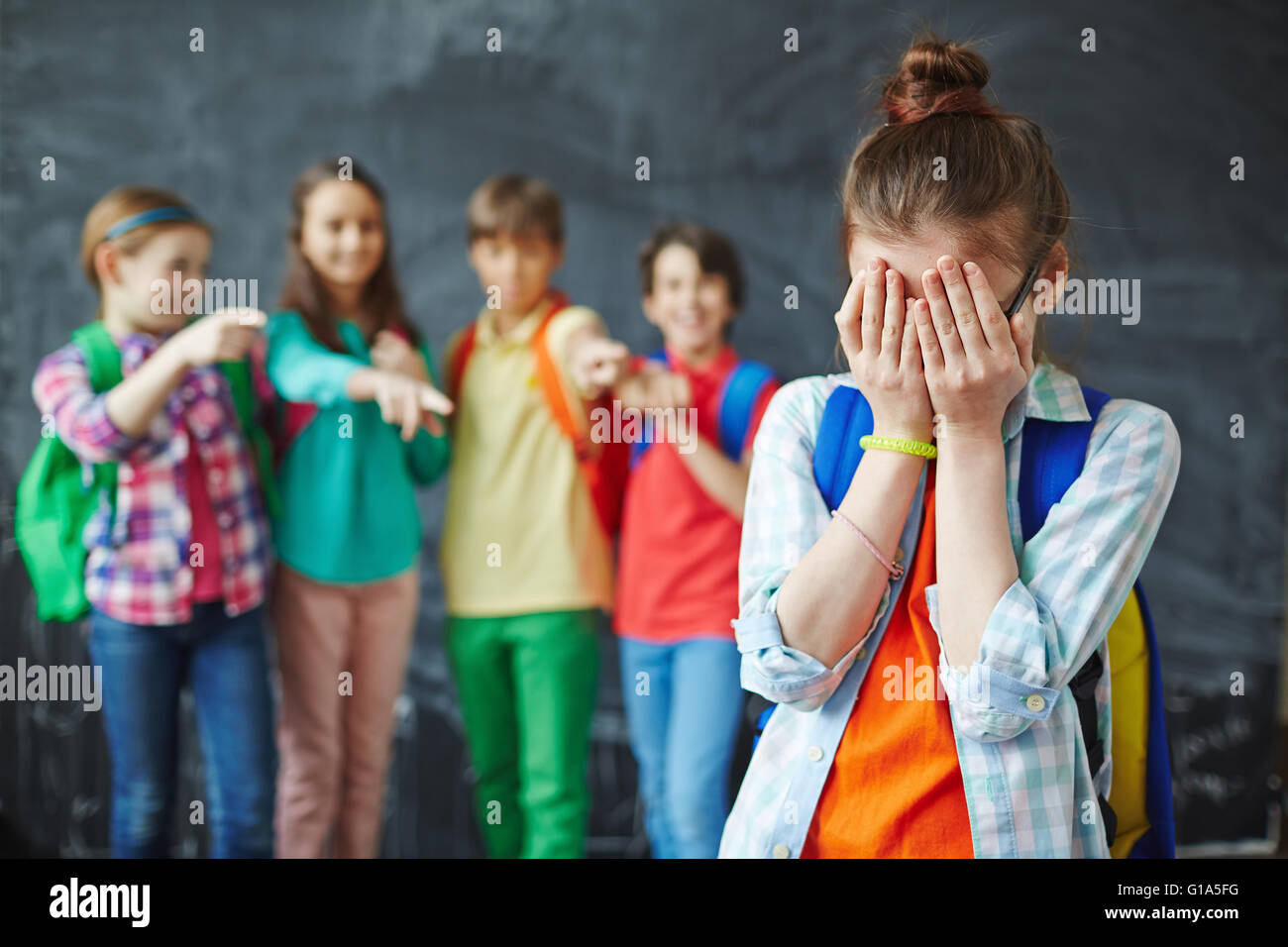 Unhappy schoolgirl crying while classmates teasing her Stock Photo