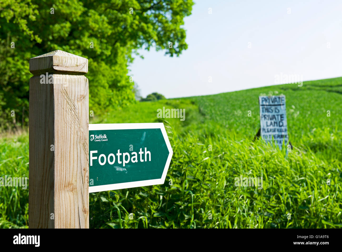 Footpath fingerpost pointing to sign in field saying this is private land, England UK Stock Photo