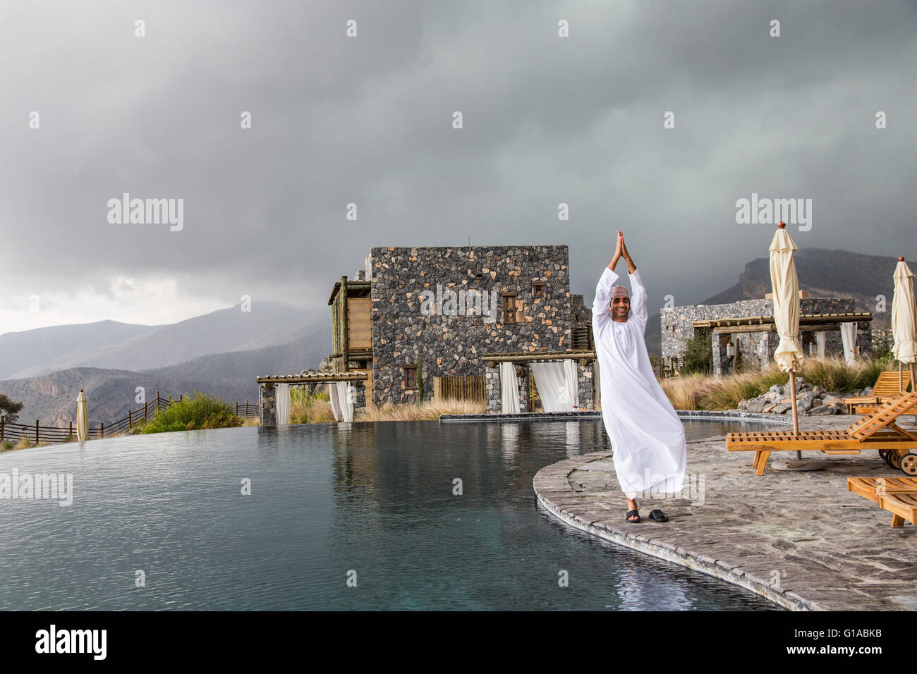 omani man in traditional clothing in a yoga pose near swimming pool at Jabal Al Akhdar Stock Photo