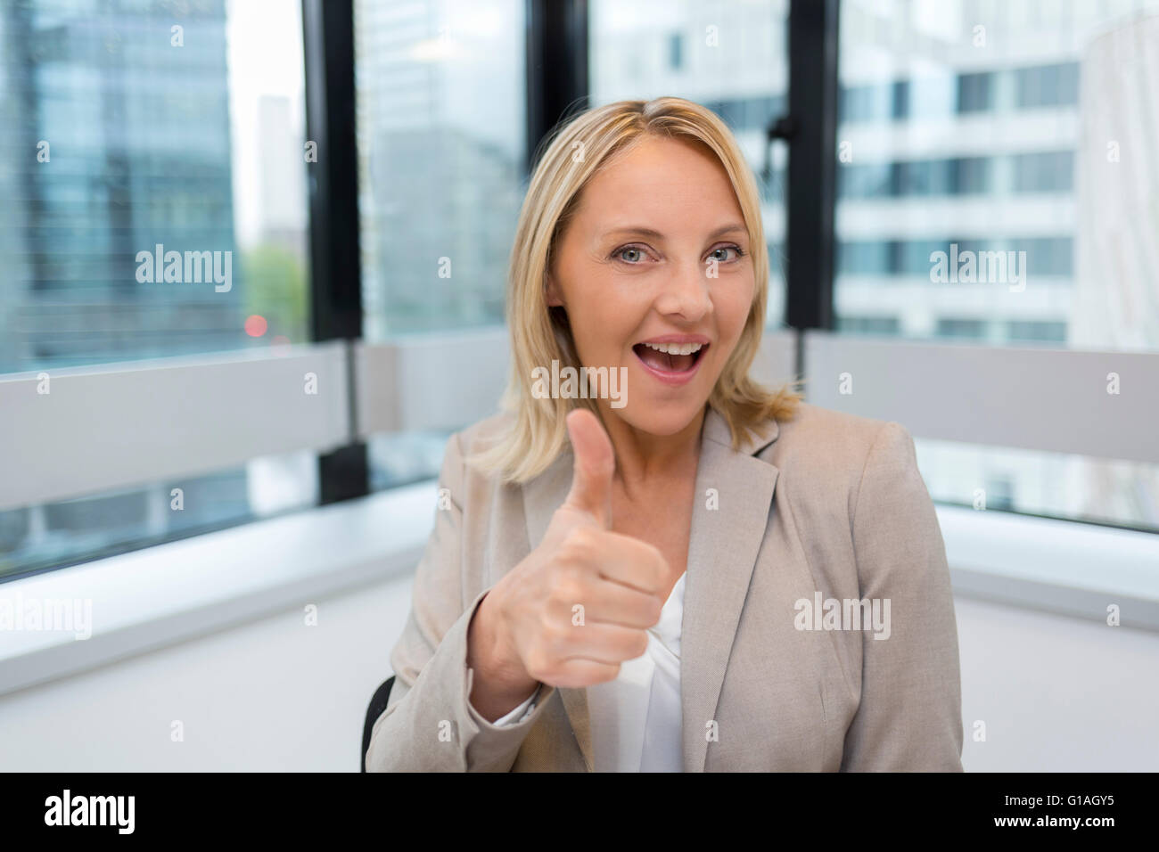 Happy Business woman thumbs up. Modern office background. Looking at camera Stock Photo