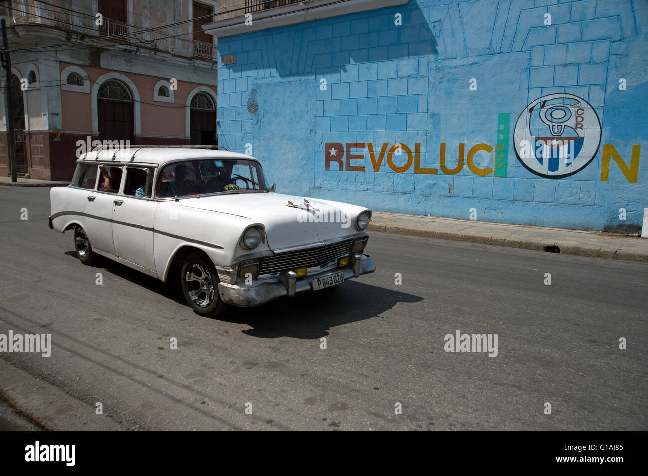 An old 1950's American classic car passes a revolution wall painting  in Cienfuegos Cuba Stock Photo