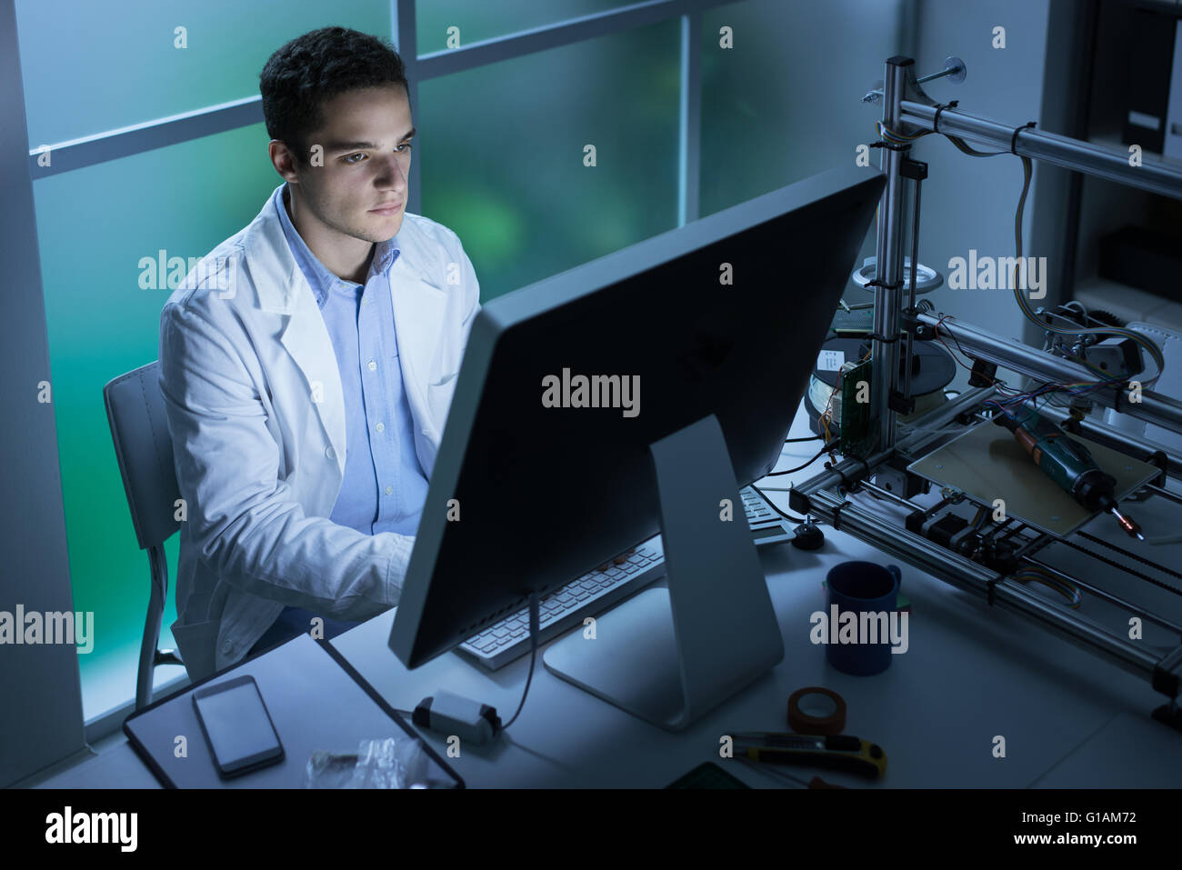 Confident engineering student working in the laboratory and using a computer, 3D printer in the background, technology and innov Stock Photo