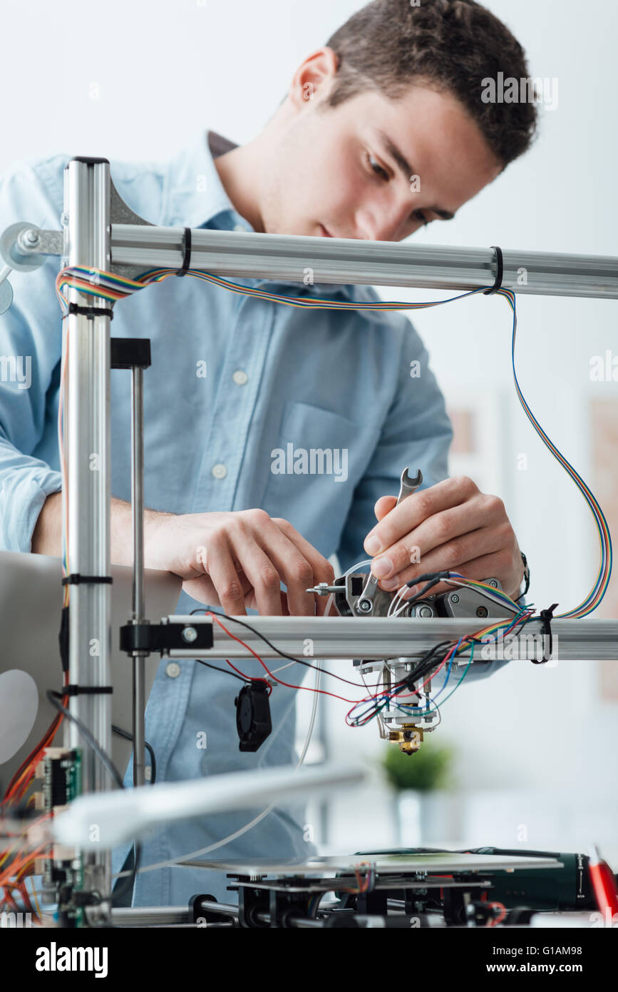 Young efficient engineer working on a 3D printer and adjusting components Stock Photo