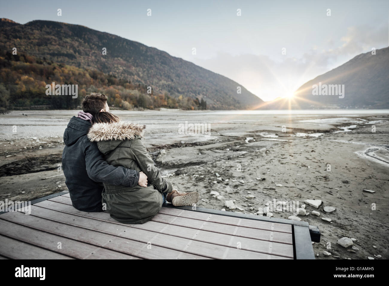 Loving couple sitting on a pier, hugging and looking away, love and feelings concept Stock Photo