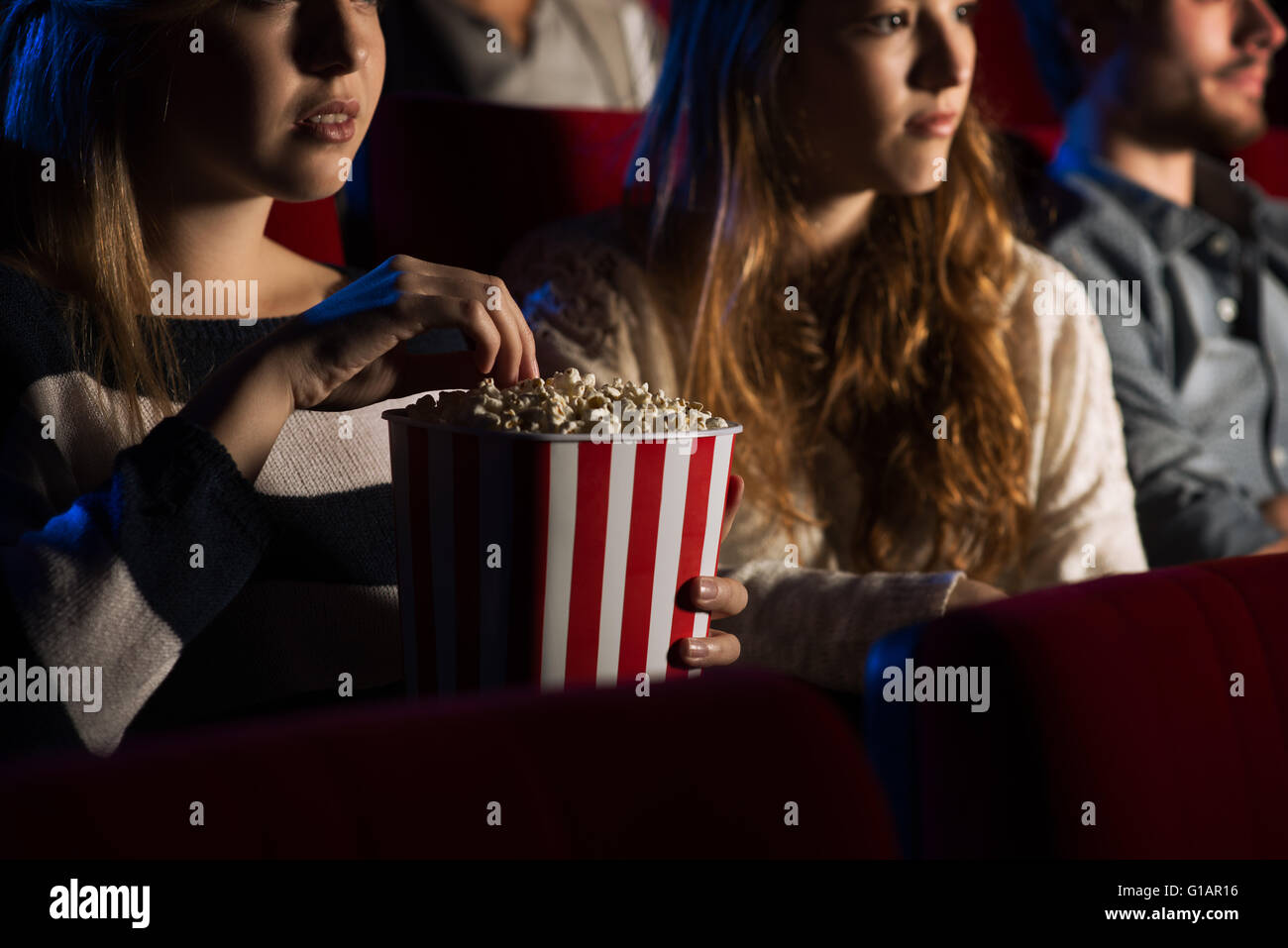 Teenager friends at the cinema watching a movie together and eating popcorn, movies and entertainment concept Stock Photo