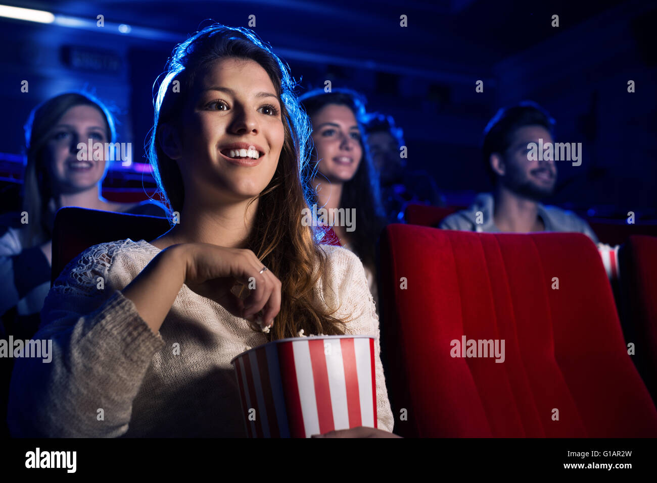 Young smiling woman watching a film in the movie theater and eating popcorn, entertainment and cinema concept Stock Photo