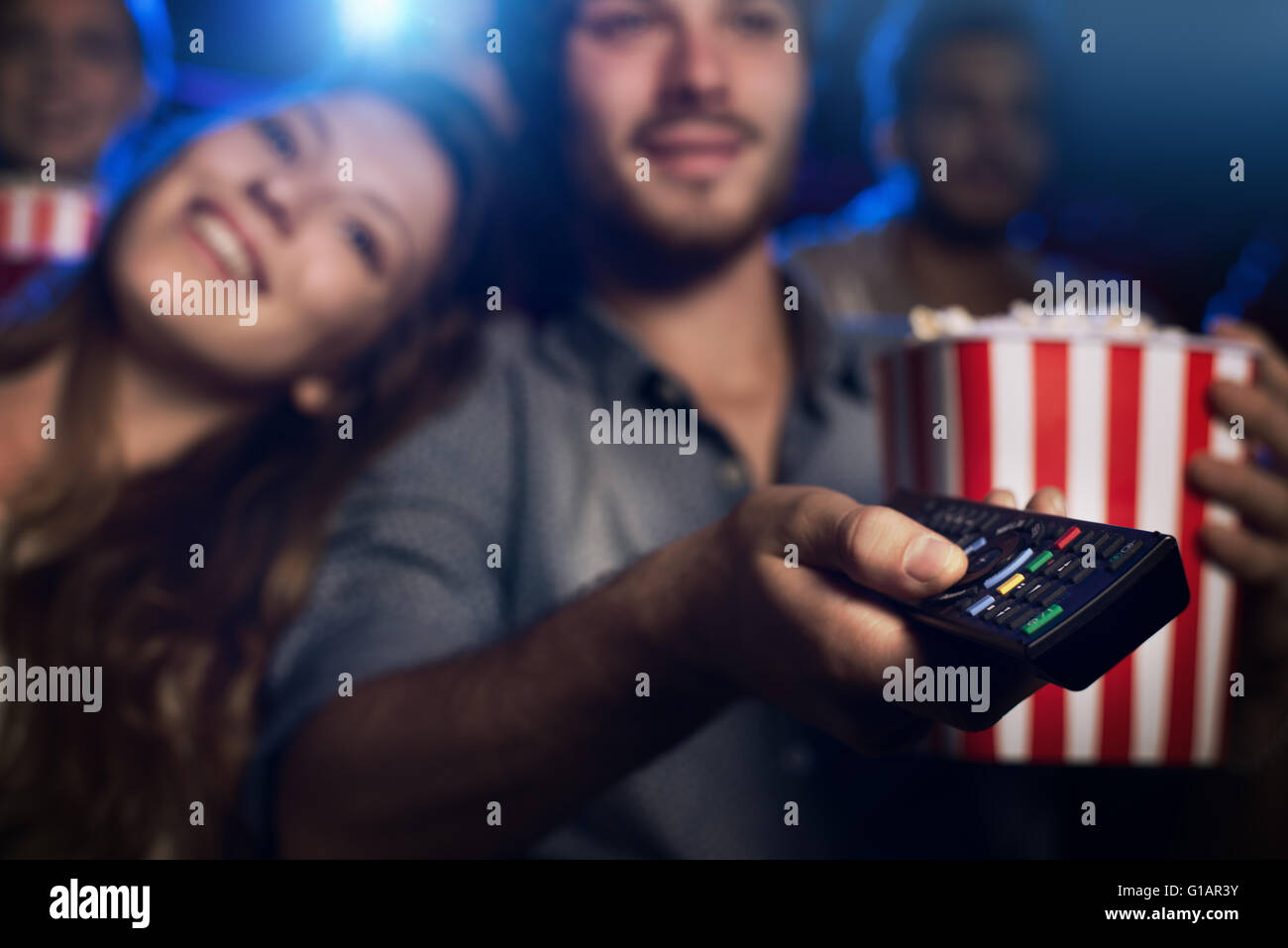 Young man watching a movie with his girlfriend and pointing a remote control: cinema, entertainment and home theater concept Stock Photo