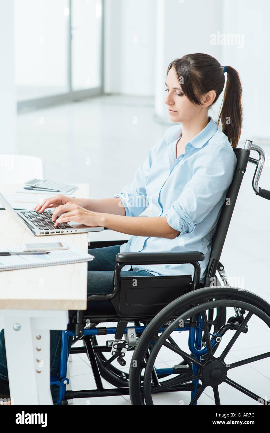 Young disabled business woman in wheelchair working at office desk and