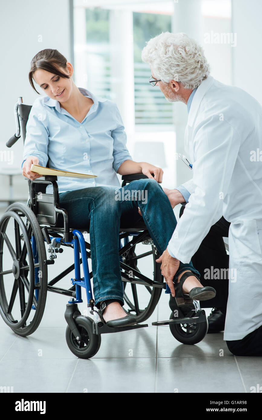 Doctor visiting an invalid woman in wheelchair, he is examining her leg