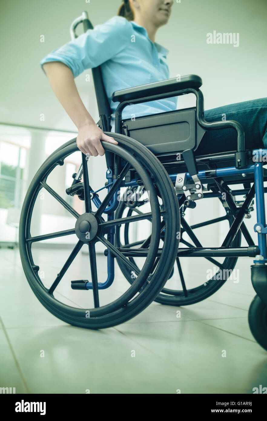 Young woman in wheelchair hand pushing on wheel close up, disability