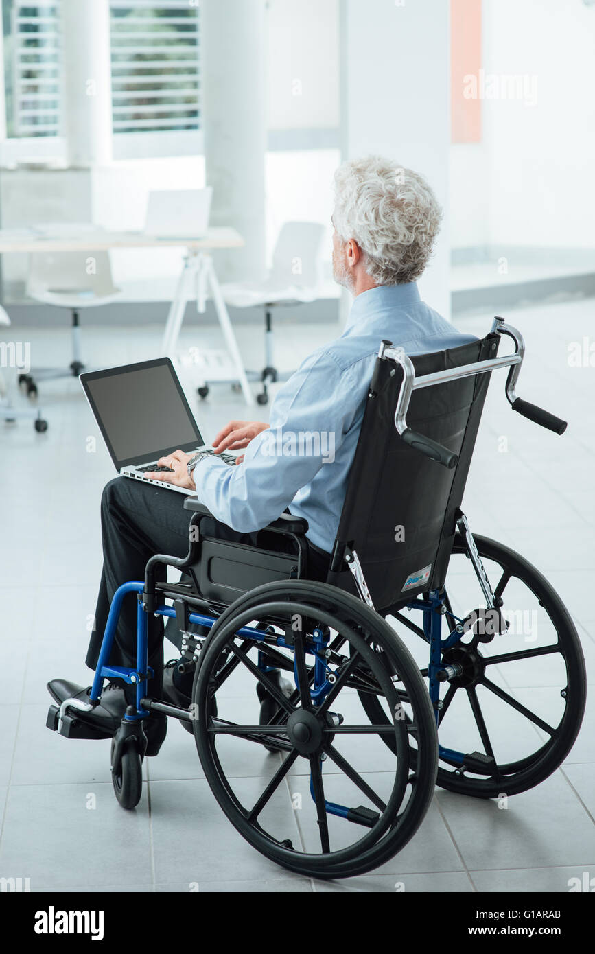 Successful corporate businessman in wheelchair at office using a laptop