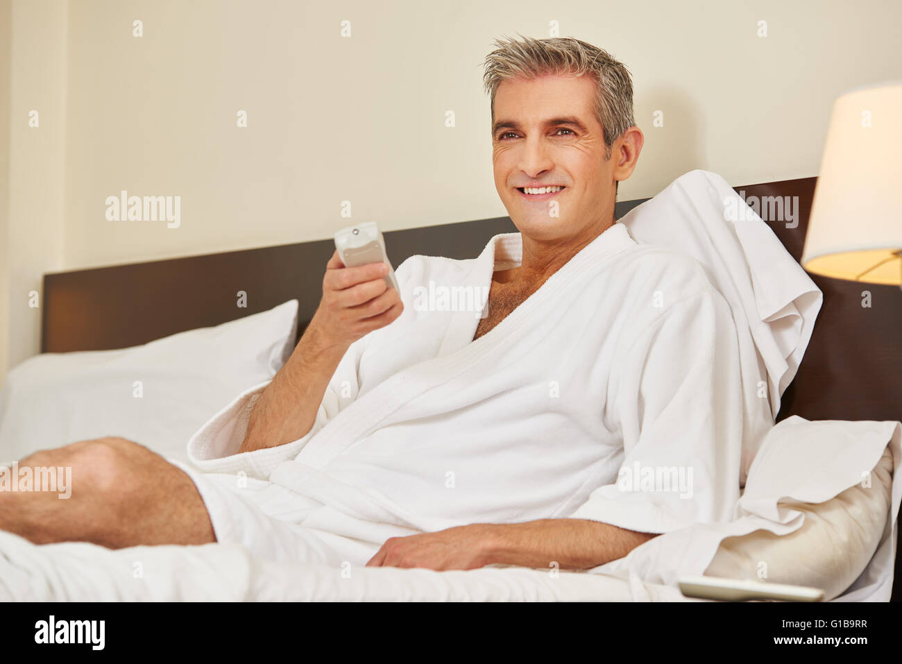 Elderly man in bathrobe watching TV in a hotel room Stock Photo