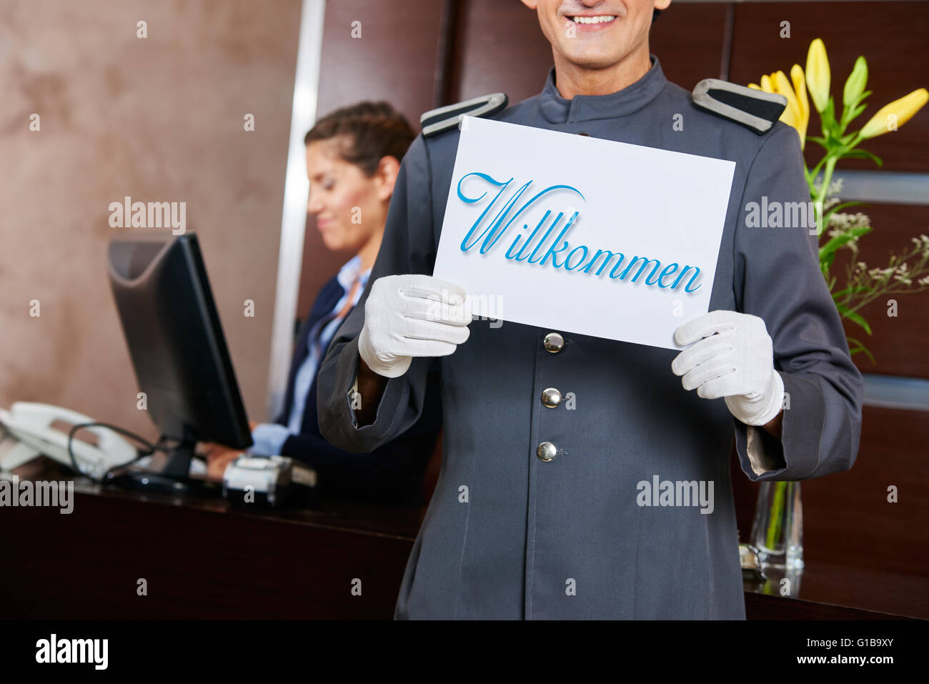 Page at hotel reception holding German sign saying "Willkommen