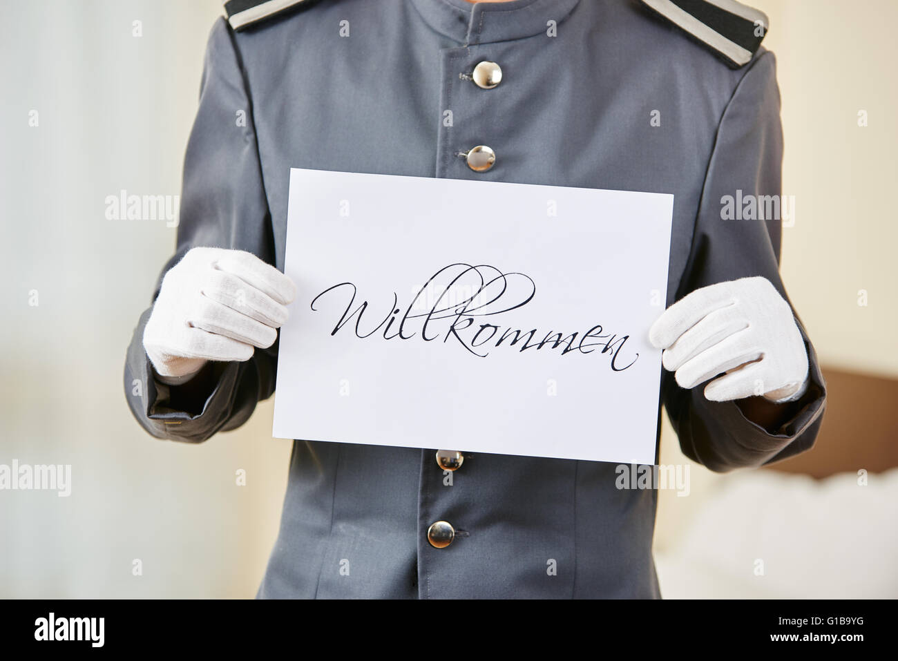 Hotel clerk holding German sign saying 'Willkommen' (welcome) Stock Photo