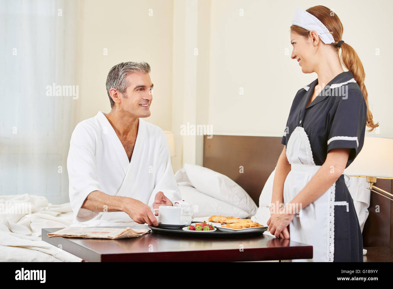 Maid bringing breakfast as room service to man in hotel room Stock Photo