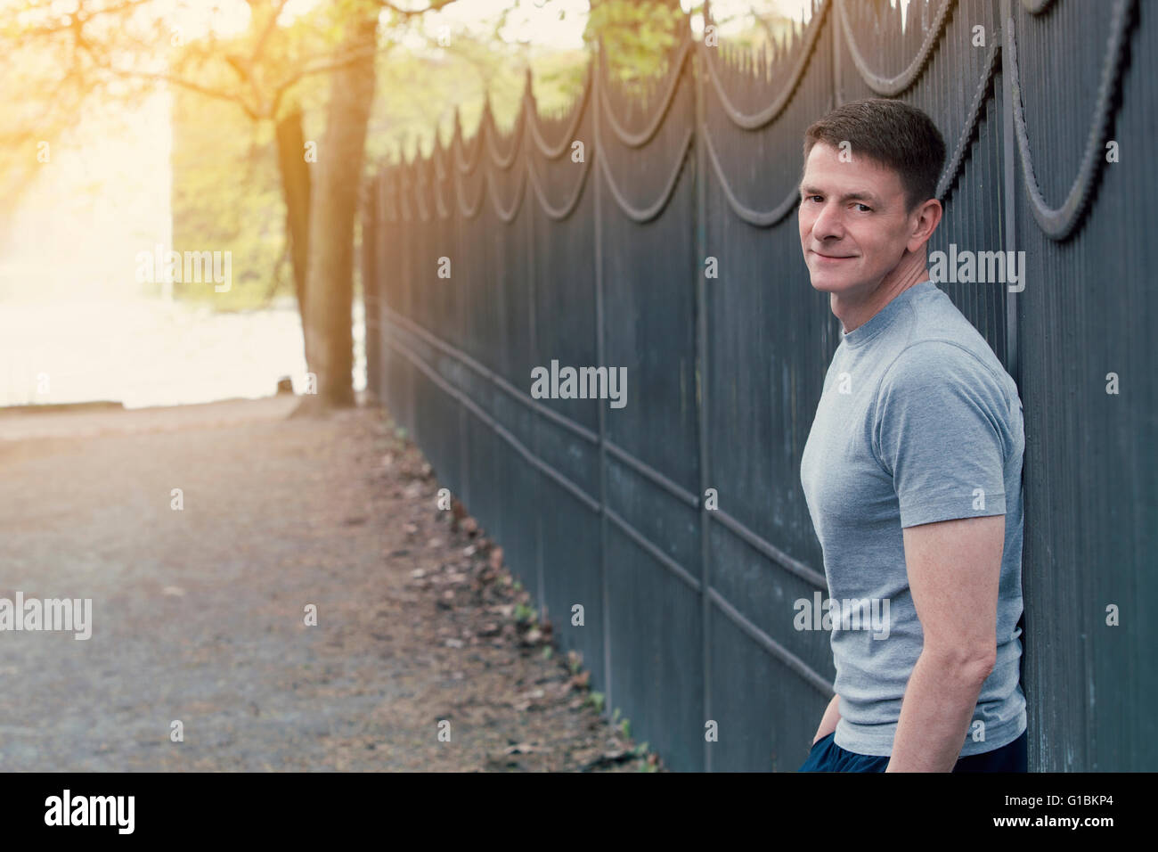 portrait of man in tshirt standing outside near a fence in nature Stock Photo