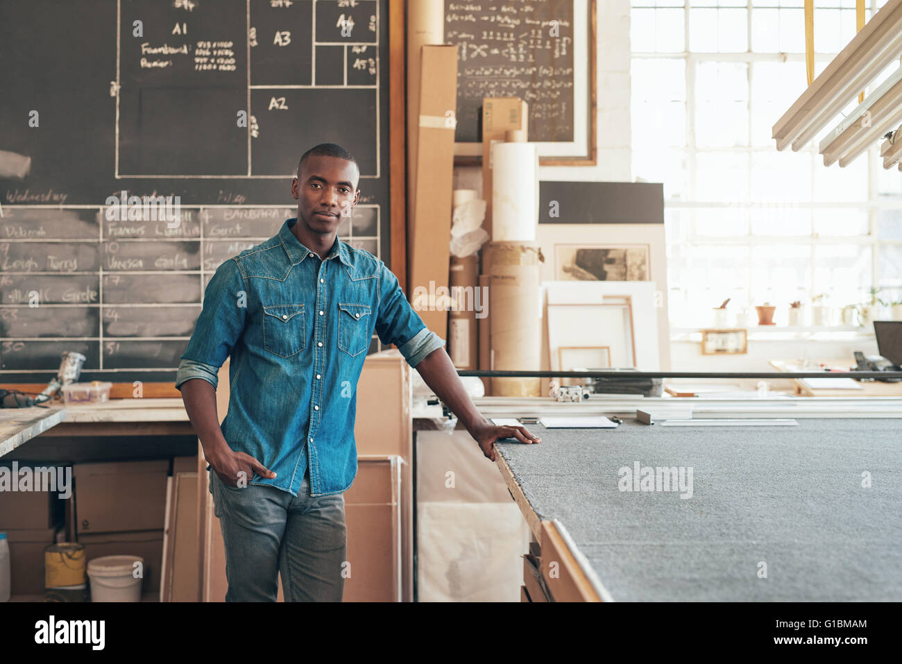 Serious young designer of African descent looking at the camera while standing casually in his studio workshop Stock Photo