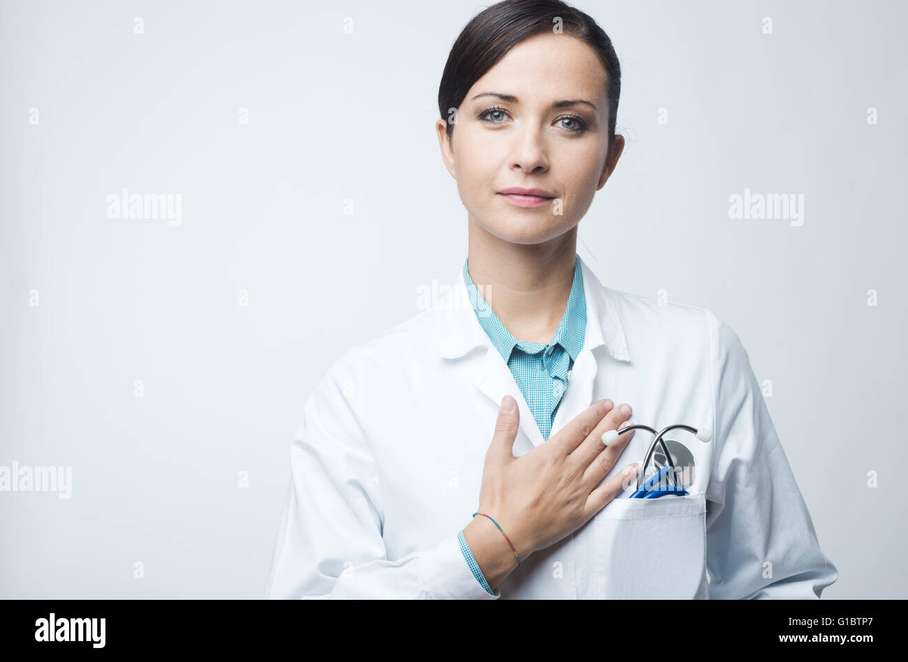 Attractive female cardiologist with stethoscope and lab coat, touching her chest. Stock Photo