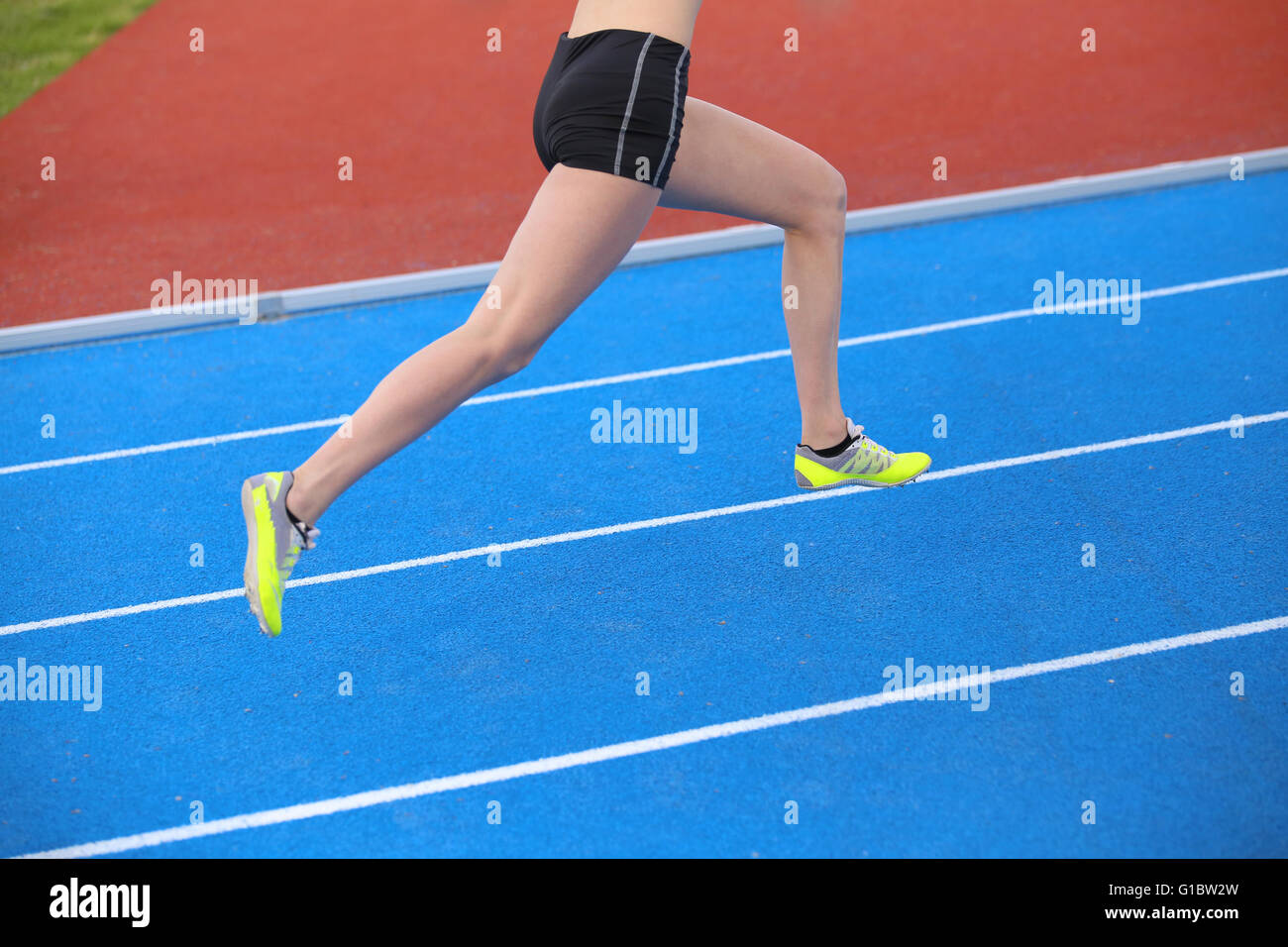 long legs of young runner running on athletic track with blue colored lanes Stock Photo