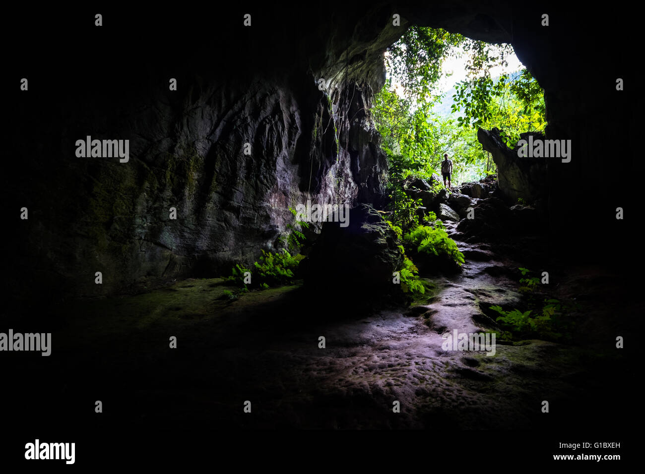A man stands and looks in through the entrance to Tham Kang Cave near Nong Khiaw in Laos Stock Photo