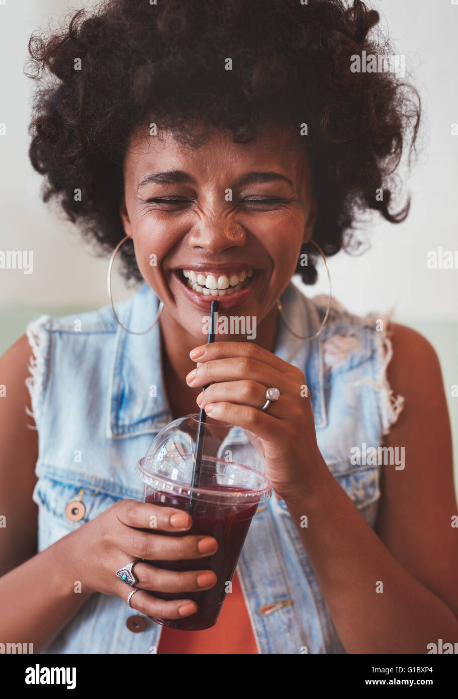 Close up portrait of cheerful young woman drinking fresh fruit juice and smiling. Happy young african female model having a drin Stock Photo